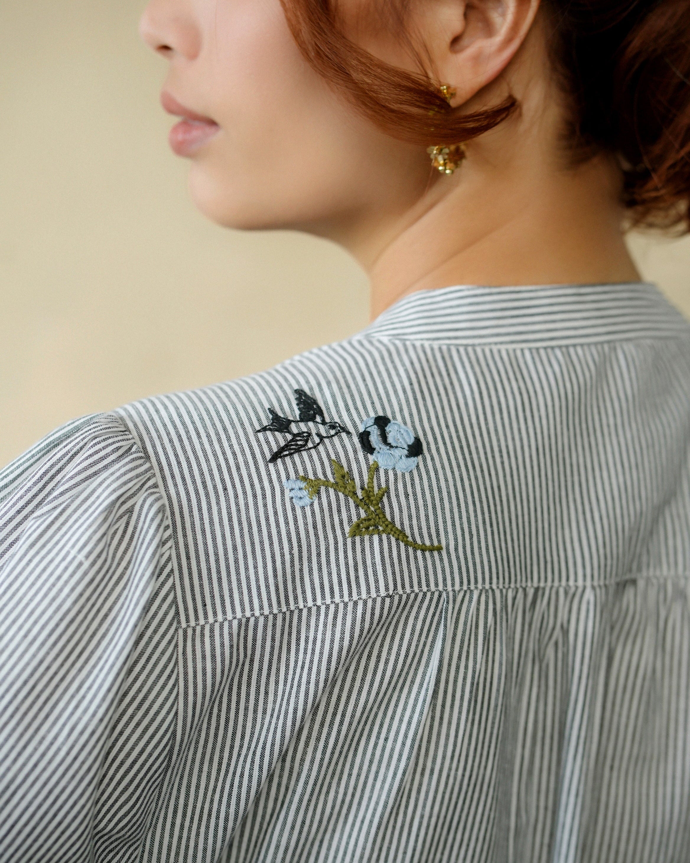 Close-up of a person wearing a striped shirt with back floral embroidery near the back collar.