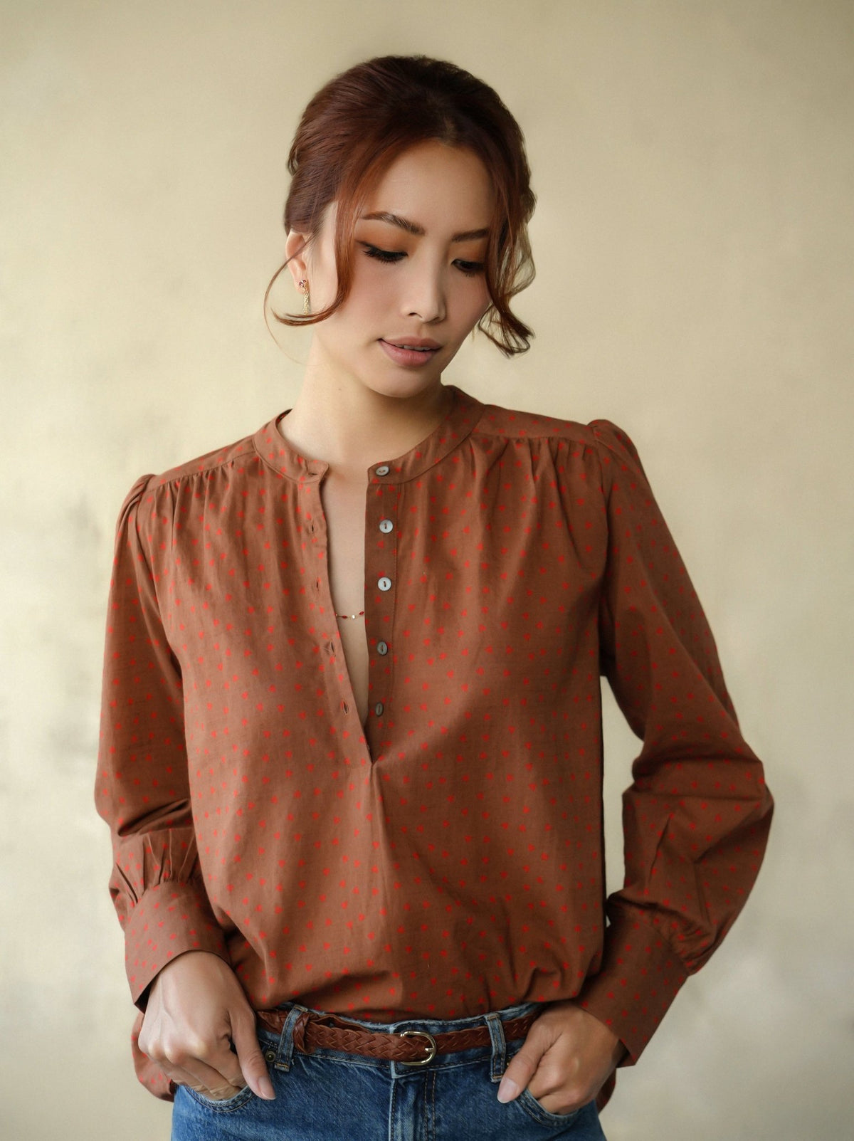 Woman wearing a brown blouse with a subtle pattern against a beige background