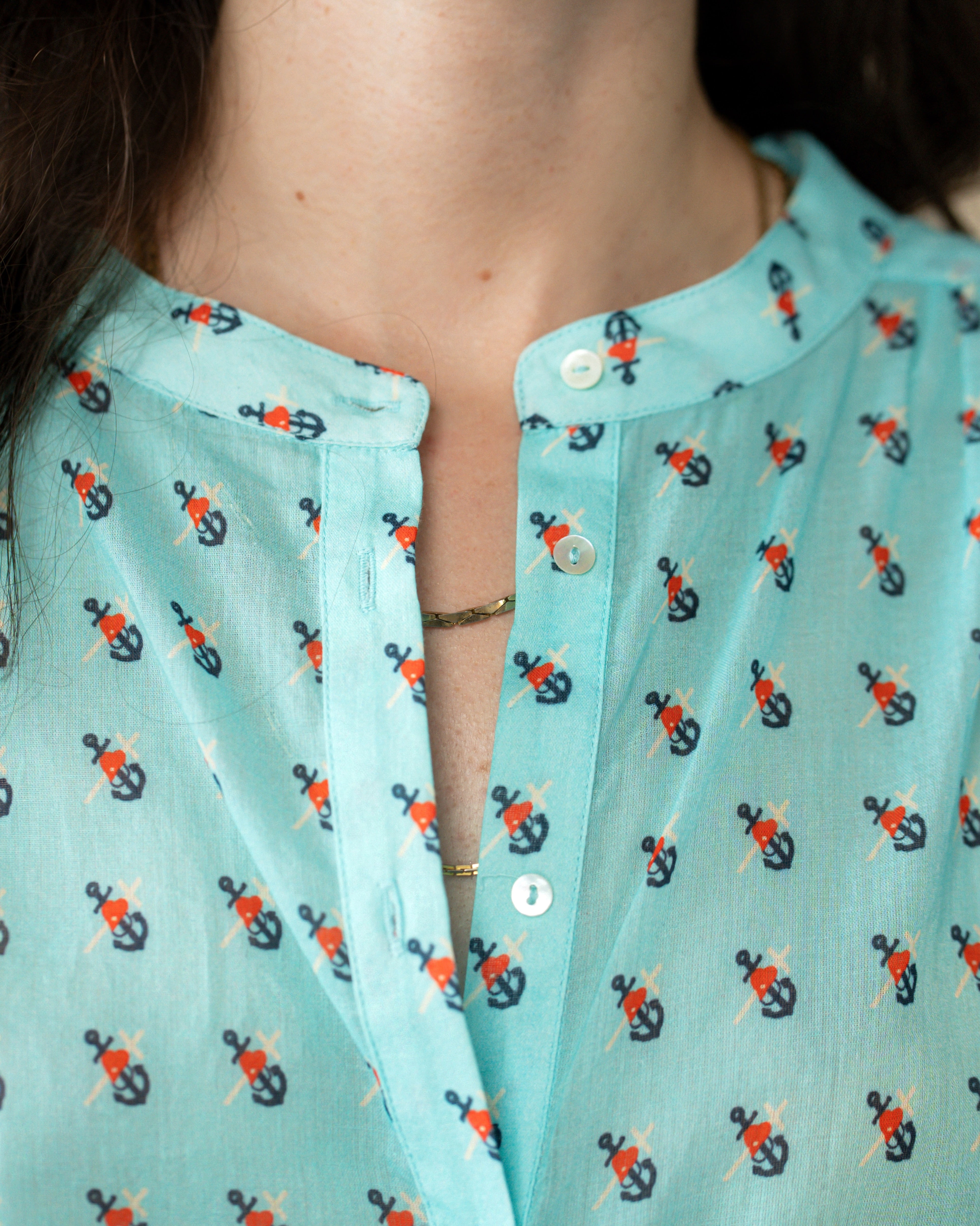 Close-up of a person wearing a mint green button-front top with a repeating anchor print in black and orange.