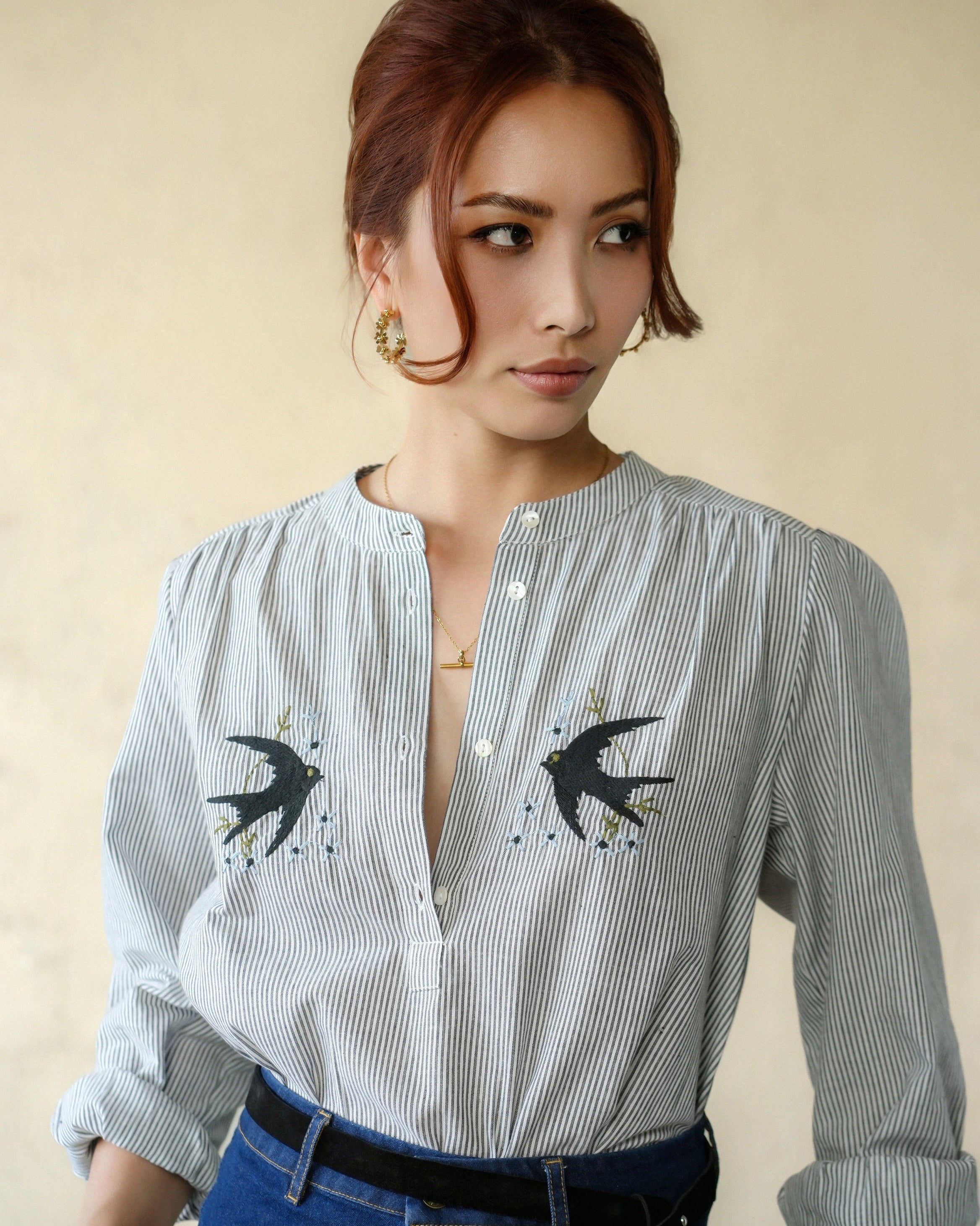 Woman wearing a white shirt with black swallow embroidery designs on a beige background