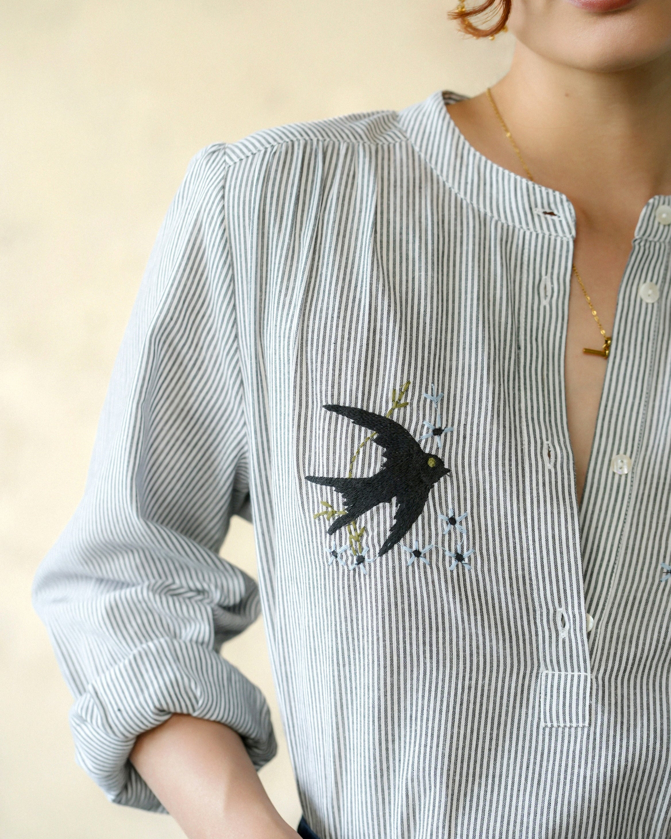 Close-up of a person wearing a striped shirt with a swallow design on a beige background