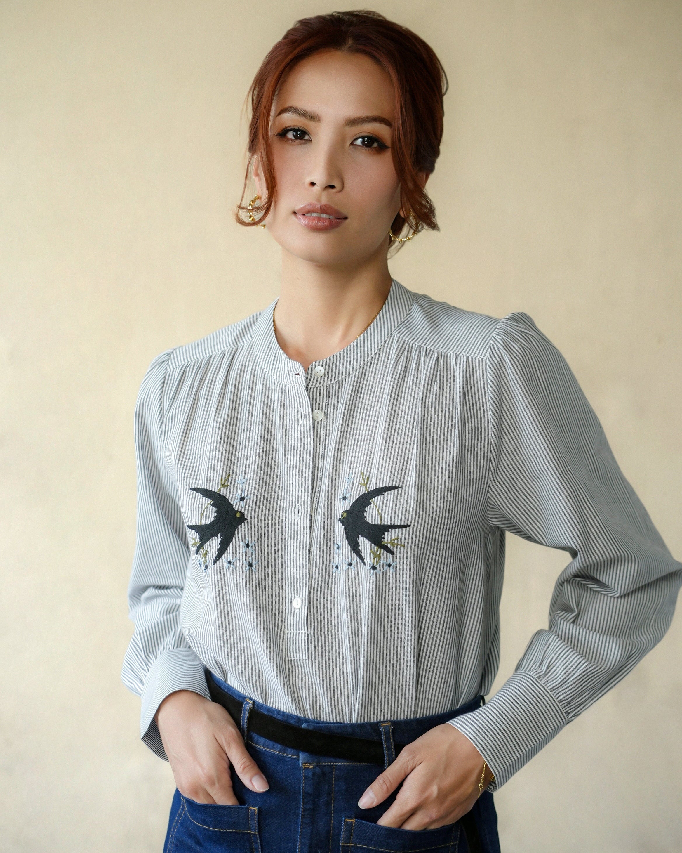 Woman wearing a grey-and-black striped shirt with swallow designs on a beige background