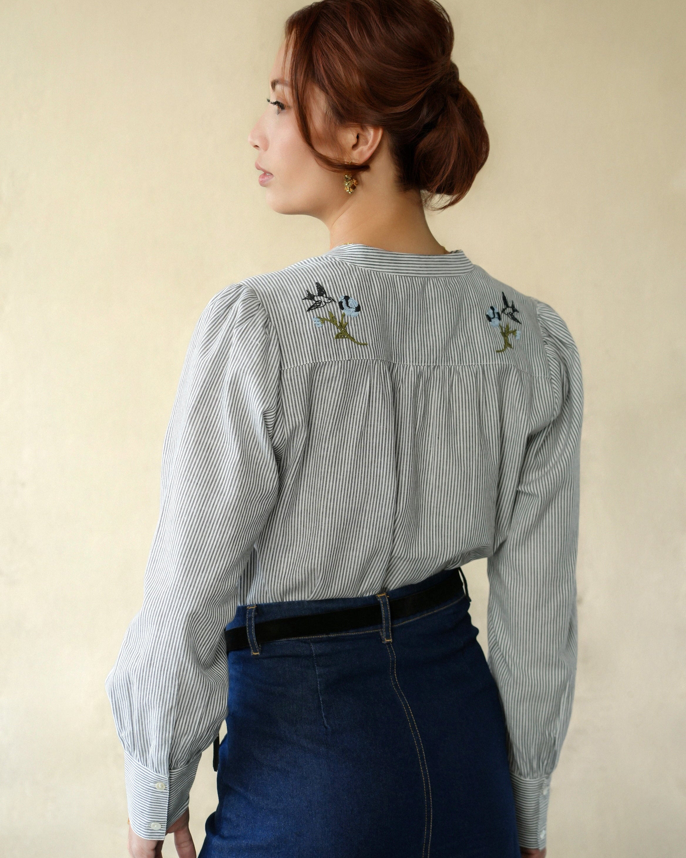 Woman wearing a grey and black striped blouse with back floral embroidery on a beige background